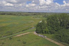 Widok z góry na Rezerwat Jeziorsko. W dole widać łąki, lasy, płynącą rzekę oraz ludzi spacerujących polna drogą