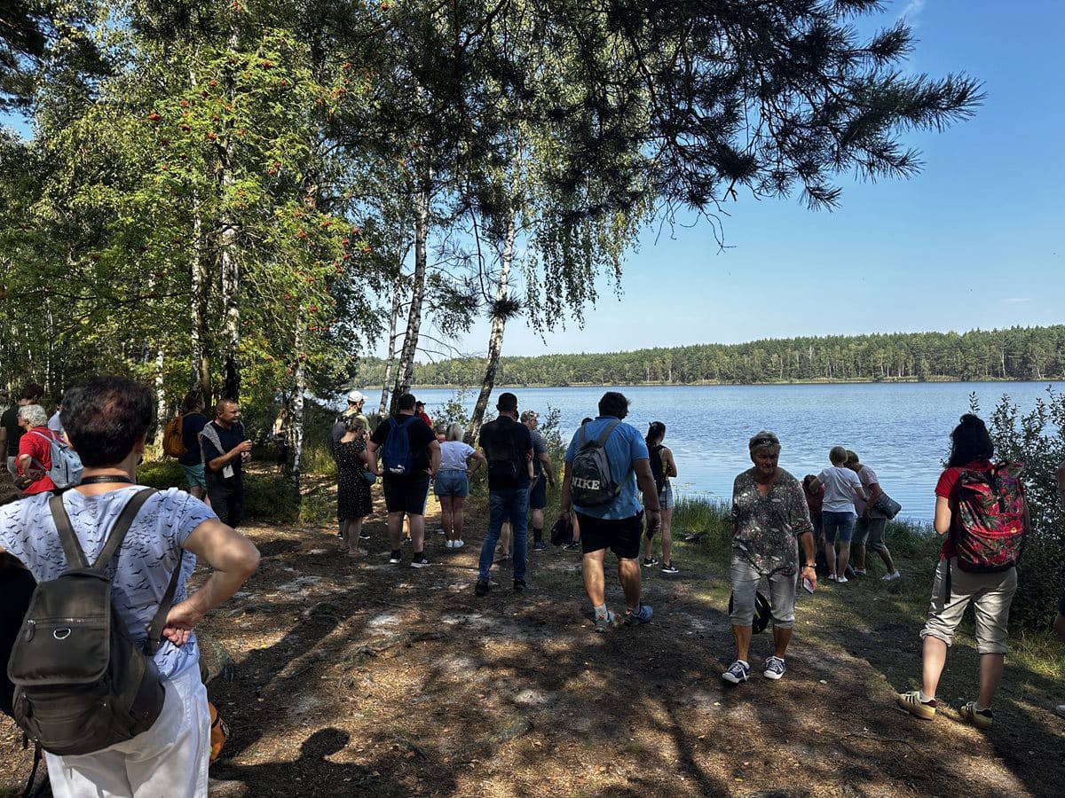 Grupa osób - turystów, stojąca w lesie nad brzegiem zbiornika wodnego